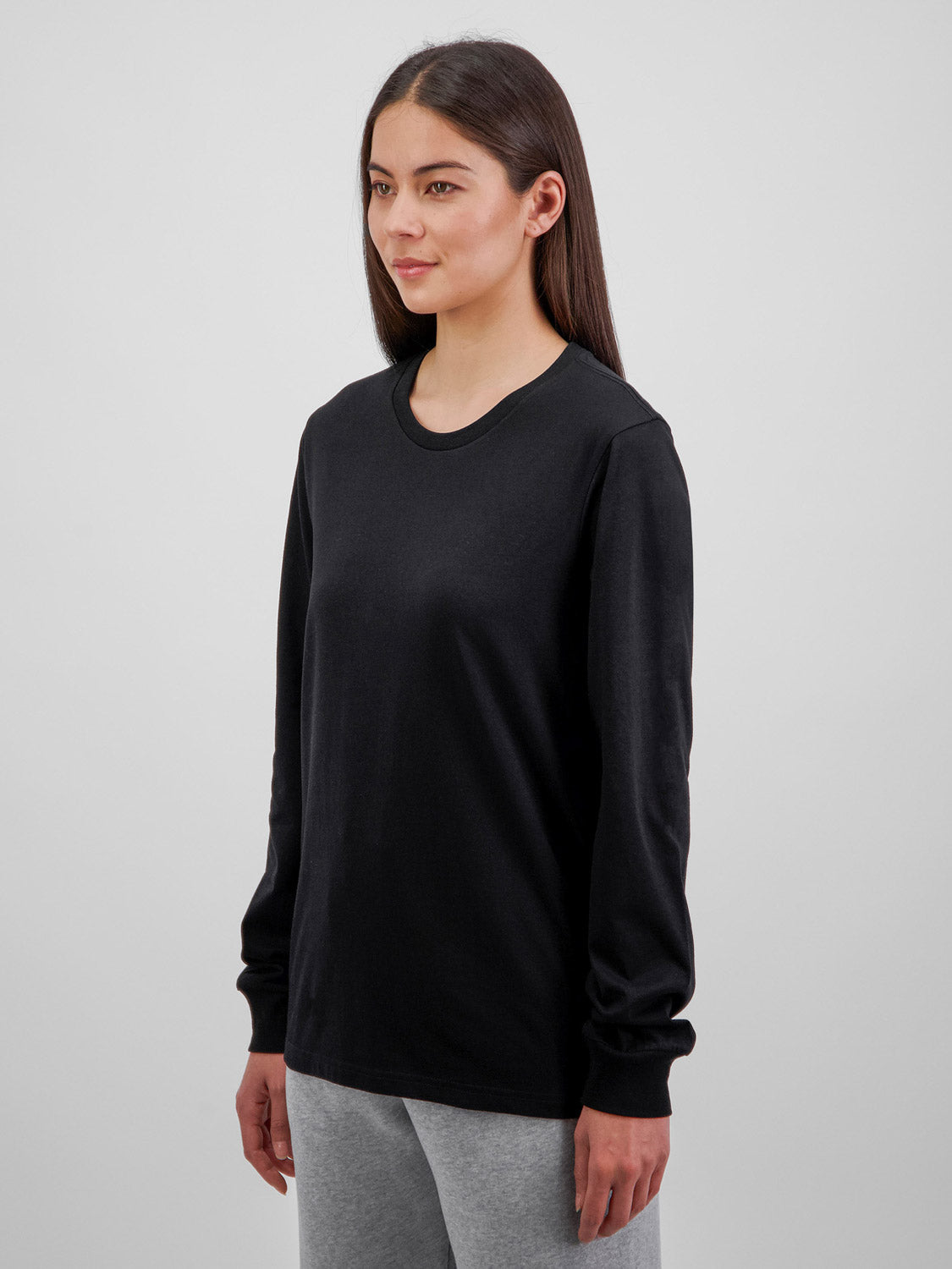 A woman wearing a black long-sleeve cotton crew neck tee with ribbed cuffs and grey pants.