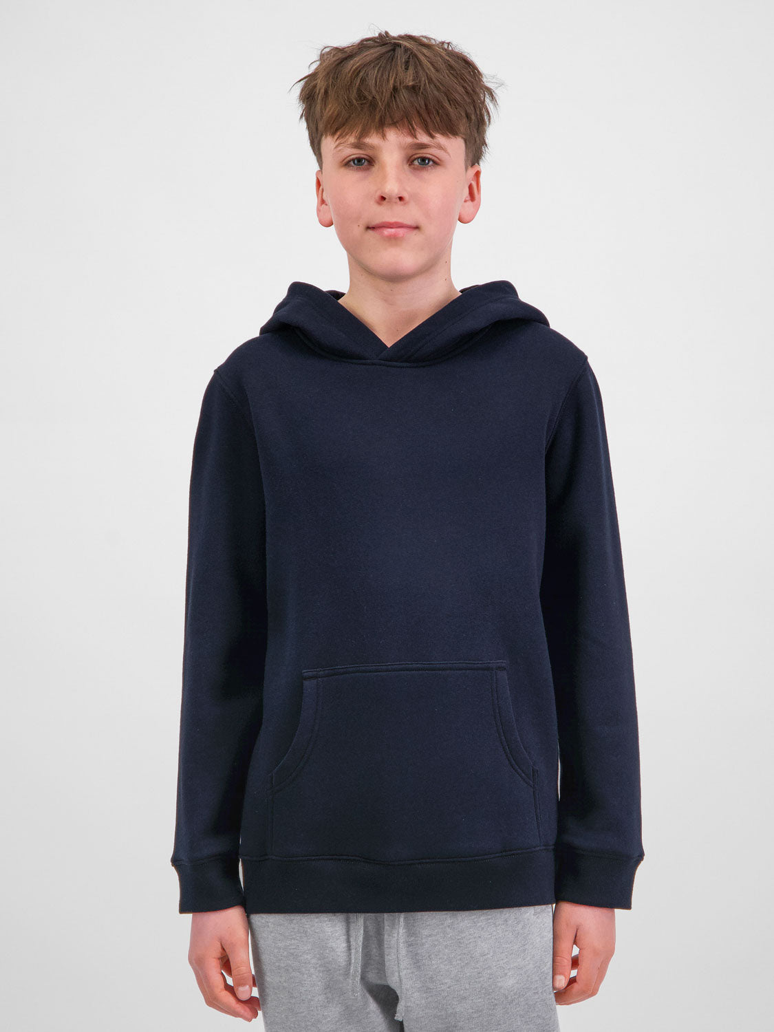 A young person wearing a navy blue Youth Basis Hoodie with a front kangaroo pocket.