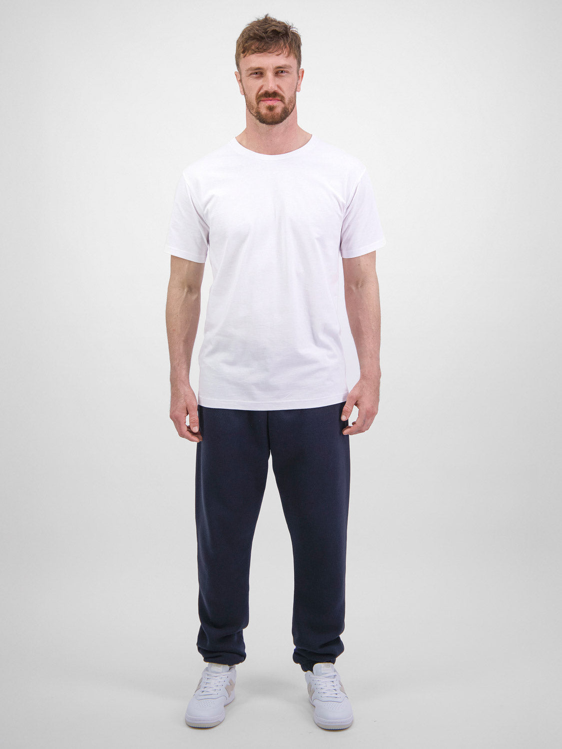A man wears navy blue Basis Track Pants with a white t-shirt and sneakers.