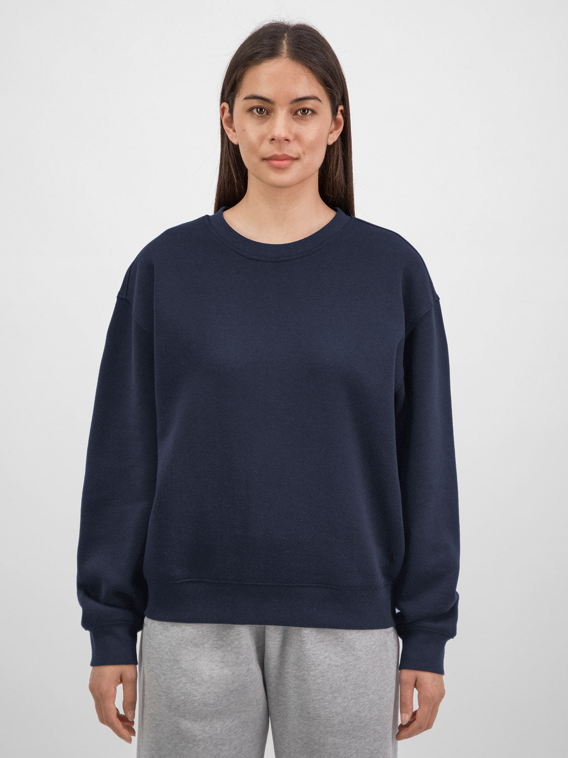 A woman wearing a navy blue crewneck sweatshirt with ribbed cuffs and a relaxed fit.