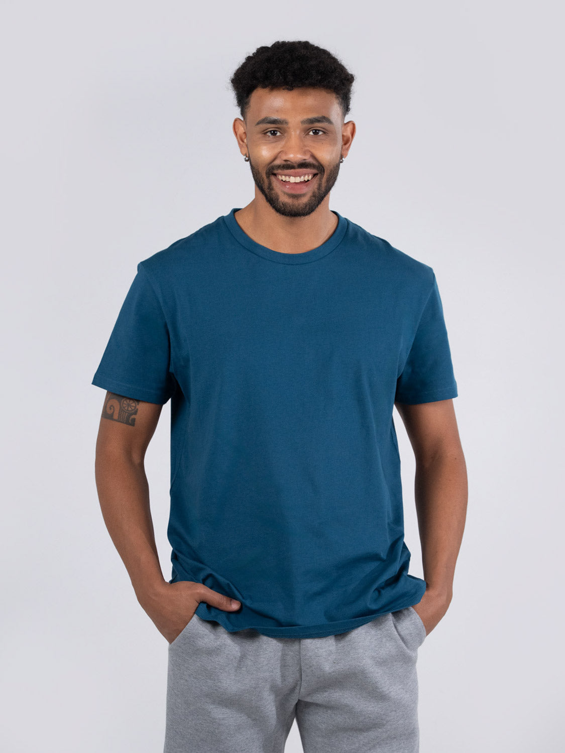 Ramo - A man wearing a teal blue crew neck t-shirt and grey sweatpants against a plain background.