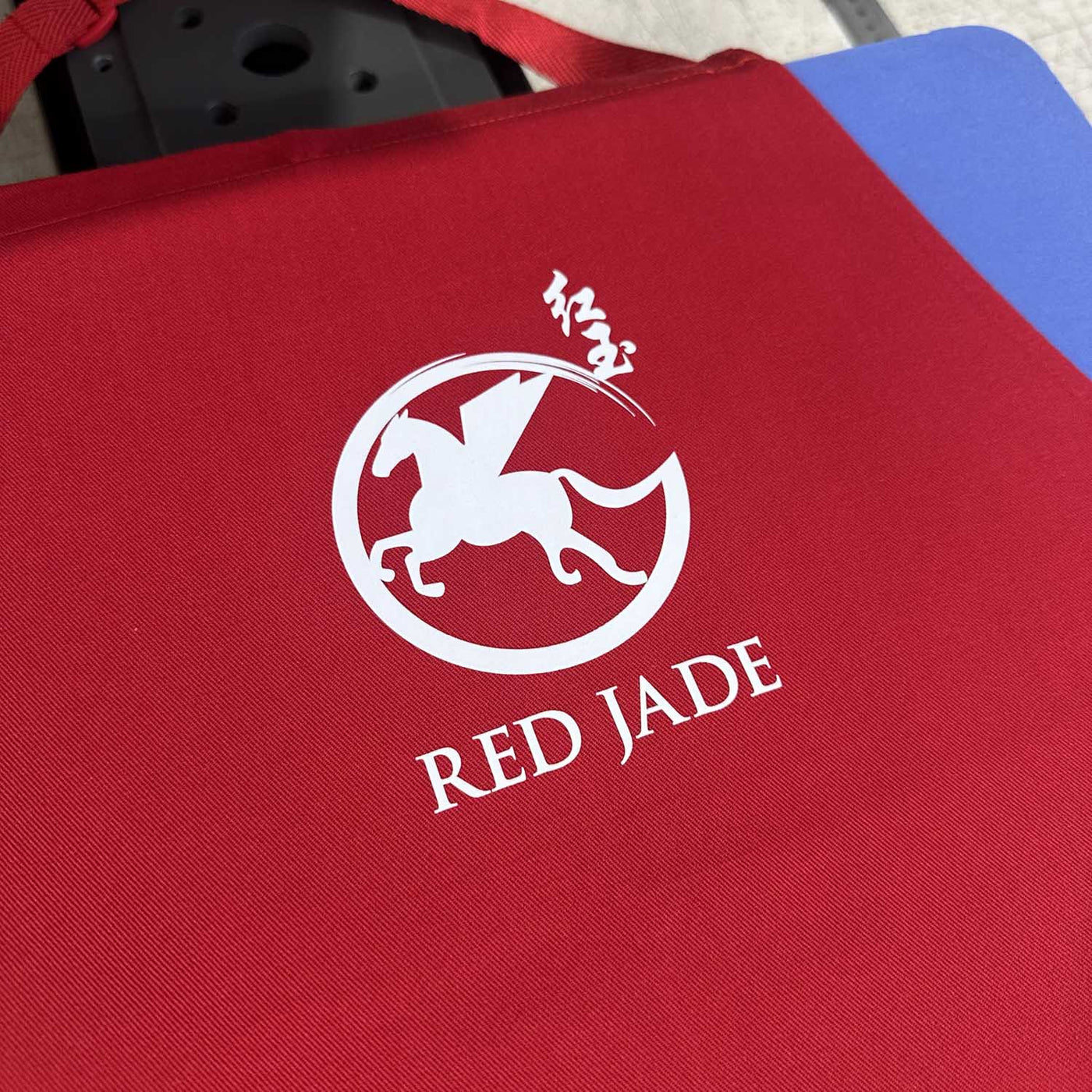 A close-up of a red fabric tote bag with a white printed logo featuring a horse and the text 'RED JADE'.
