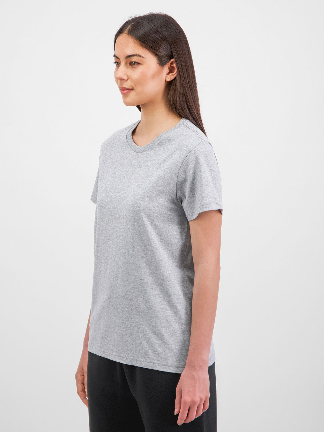 A woman wearing a grey short sleeve cotton t-shirt and black pants against a white background.