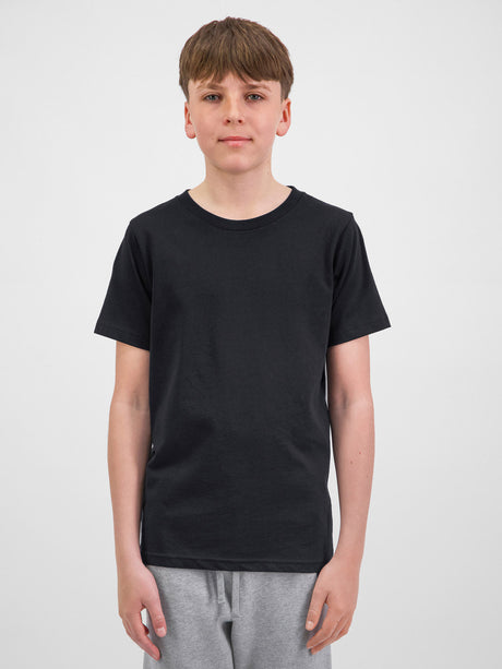 A young person wearing a black Youth Basis Short Sleeve Tee and grey sweatpants.