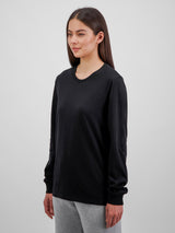 A woman wearing a black long-sleeve cotton crew neck tee with ribbed cuffs and grey pants.