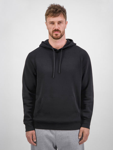 A man wearing a black Mens Basis Hoodie with a front kangaroo pocket and adjustable drawcord.