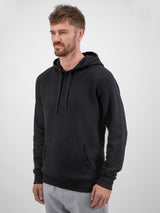 A man wears a black Mens Basis Hoodie with a front kangaroo pocket and adjustable drawcord.