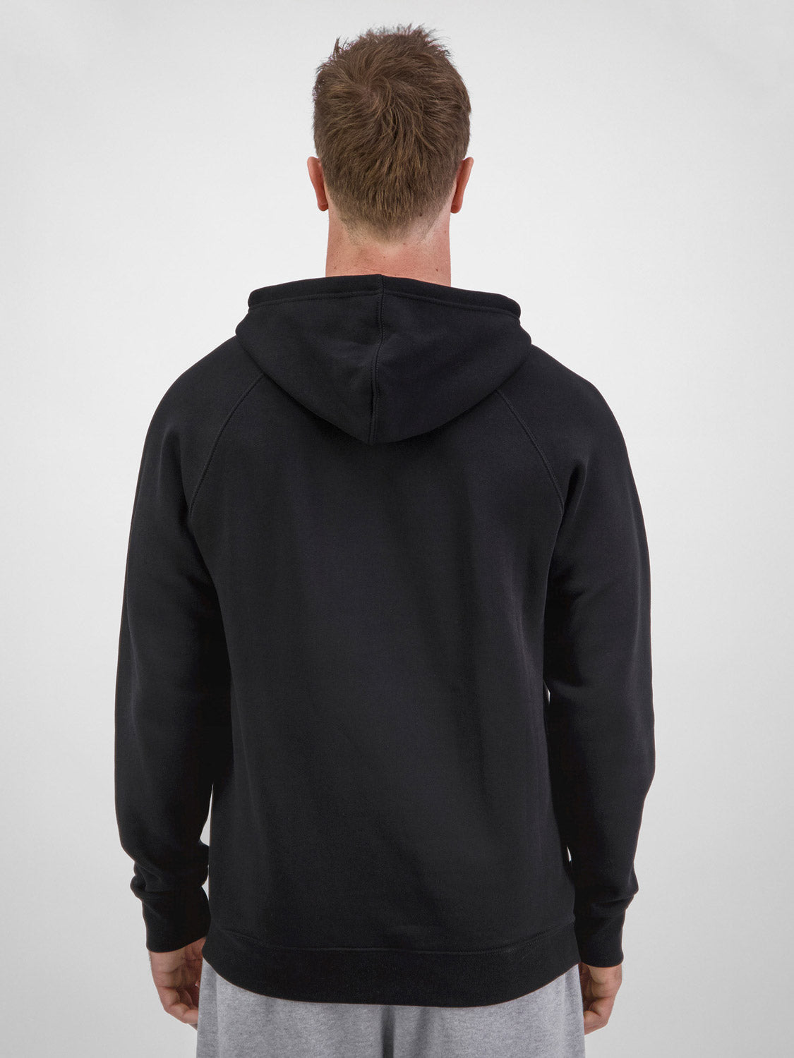 Rear view of a man wearing a black Basis Hoodie with raglan sleeves and a hood.