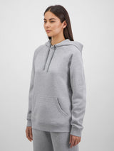 A woman wears a grey marle Basis Hoodie with a kangaroo pocket and adjustable drawcord hood.