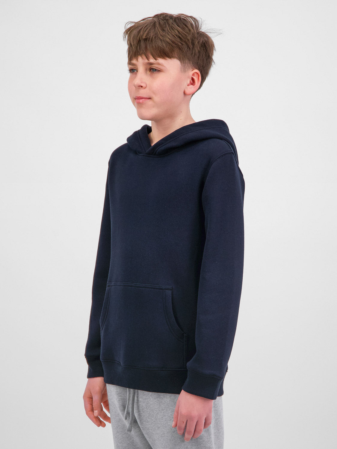 A young person wearing a navy blue Youth Basis Hoodie with a front kangaroo pocket.
