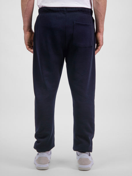 Rear view of a man wearing navy blue Basis Track Pants with a back pocket and elasticated cuffs.