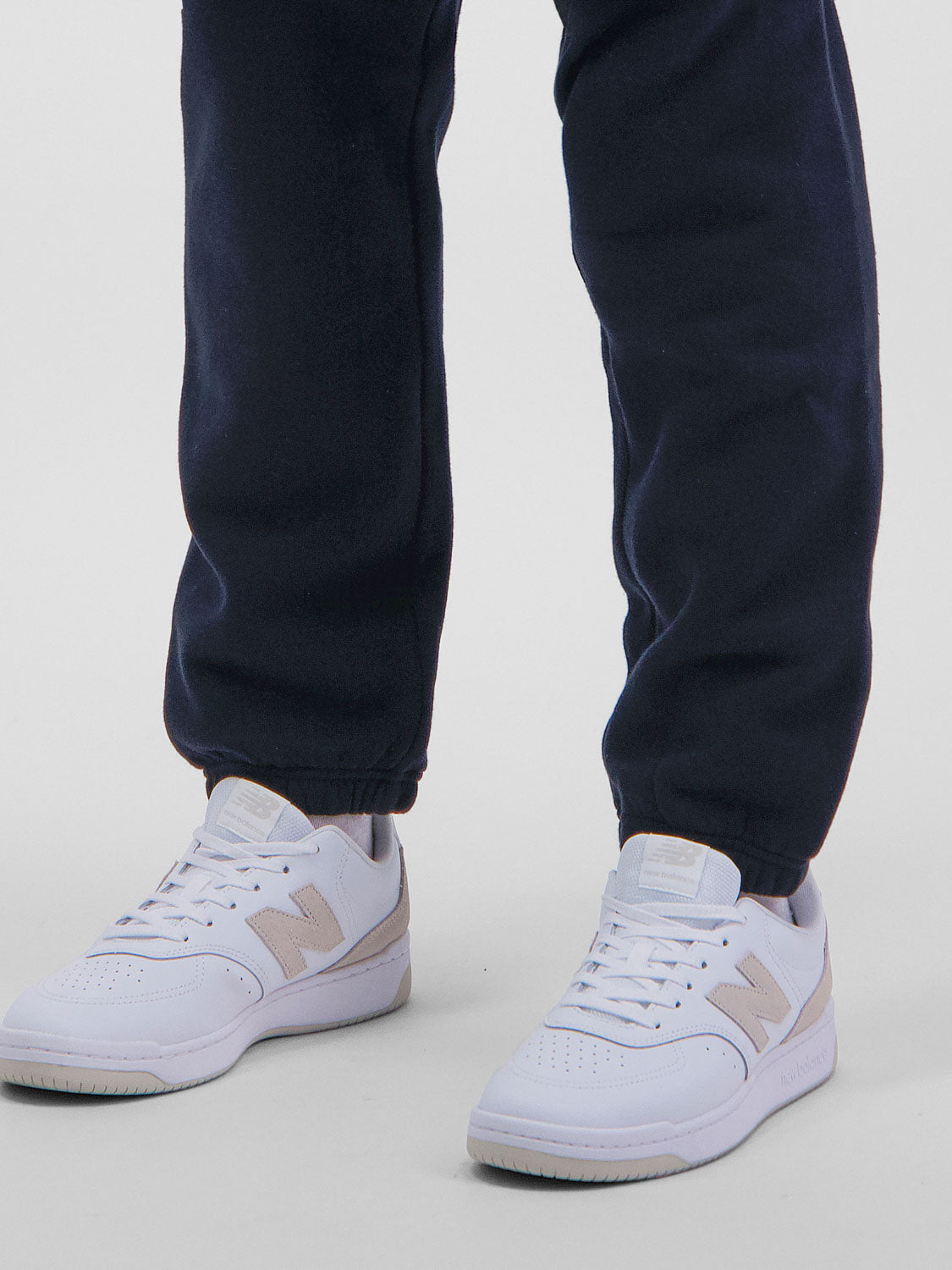 A person wearing navy blue Mens Basis Track Pants with elasticated ankle cuffs and white sneakers.