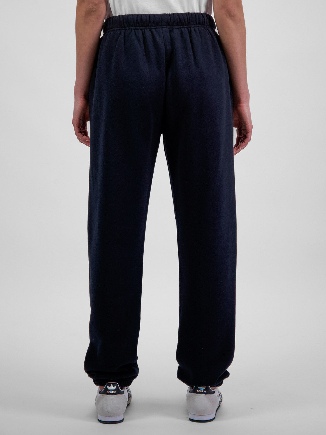 Rear view of a person wearing navy blue relaxed-fit fleece track pants with elastic cuffs.