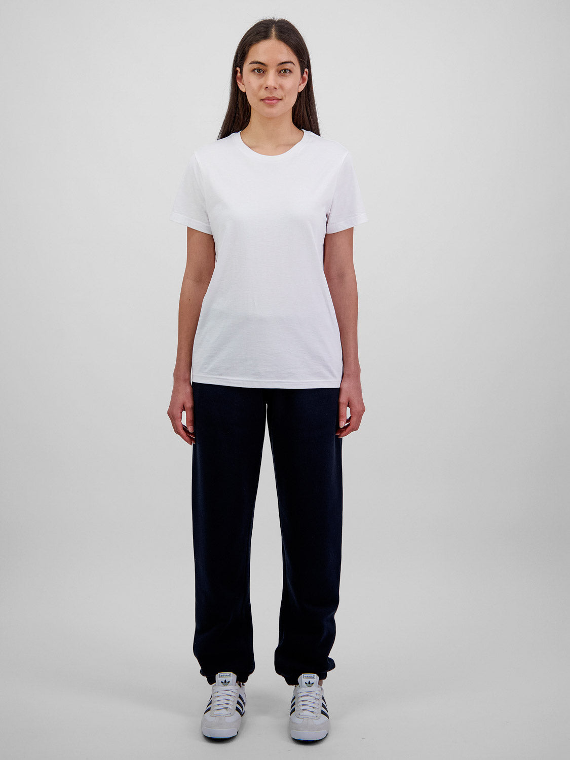 A woman wears navy blue Womens Basis Track Pants with a white t-shirt and sneakers.