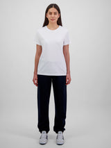 A woman wears navy blue Womens Basis Track Pants with a white t-shirt and sneakers.