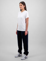 A woman stands wearing navy blue relaxed-fit track pants with elastic cuffs and a white t-shirt.