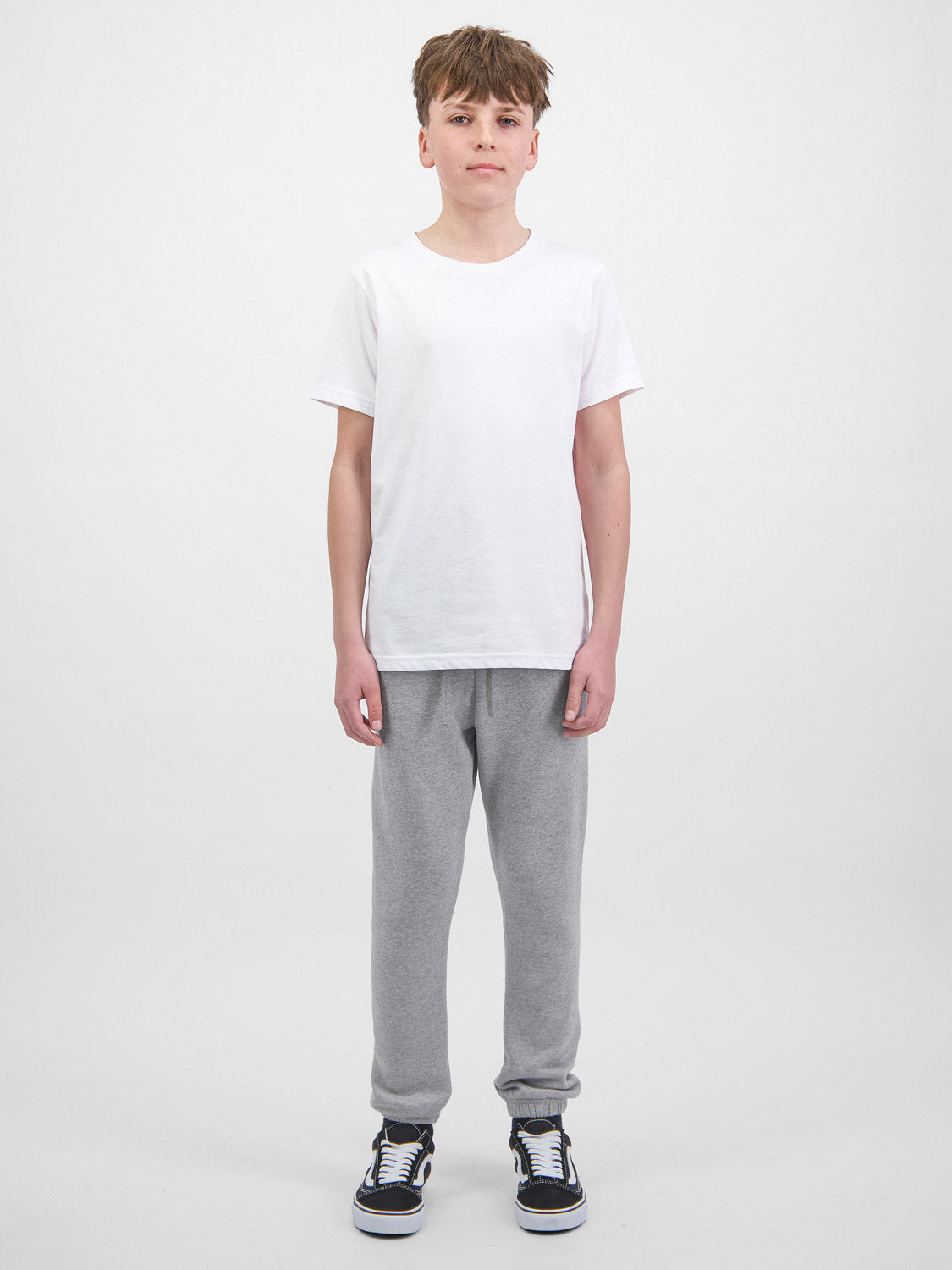 A young person wearing grey Youth Basis Track Pants with an elastic waist and cuffed ankles.