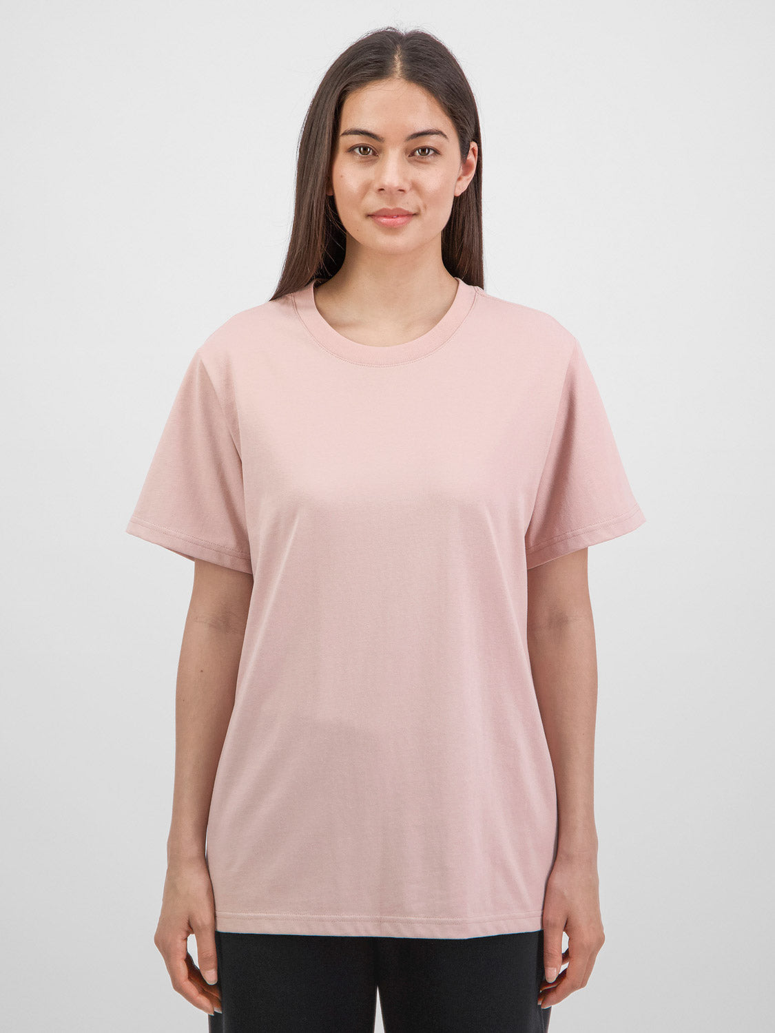 A woman wearing a relaxed-fit, light pink short sleeve crew neck t-shirt.