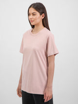 A woman wears a light pink, relaxed-fit short sleeve cotton tee with a ribbed crew neckline.