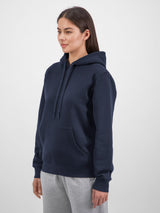 A woman wearing a navy blue mid-weight everyday hoodie with a front pocket and drawstring hood.