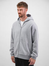 A man wears a light grey, relaxed-fit zip-up hoodie with a front pocket and ribbed cuffs.