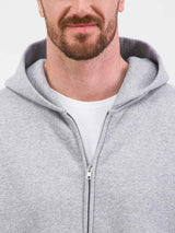 Close-up of a man wearing a grey zip-up hoodie with a white t-shirt underneath.