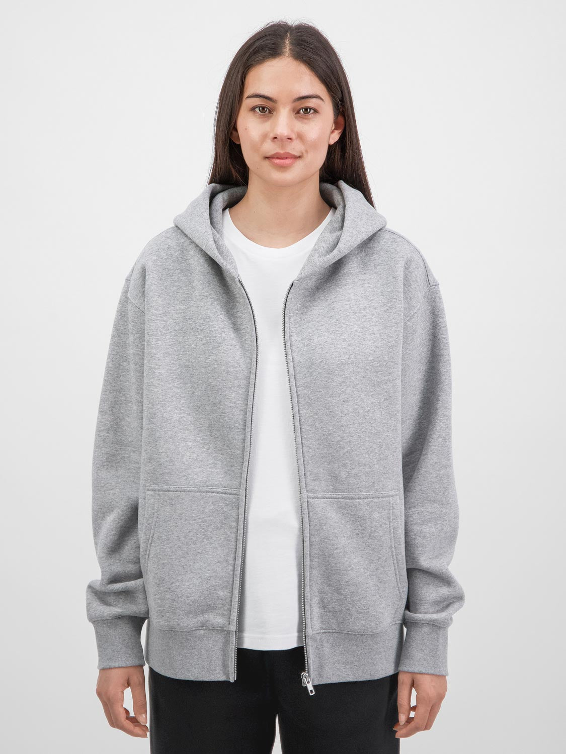 A woman wears a relaxed-fit grey zip-up hoodie with front pockets and a white t-shirt.