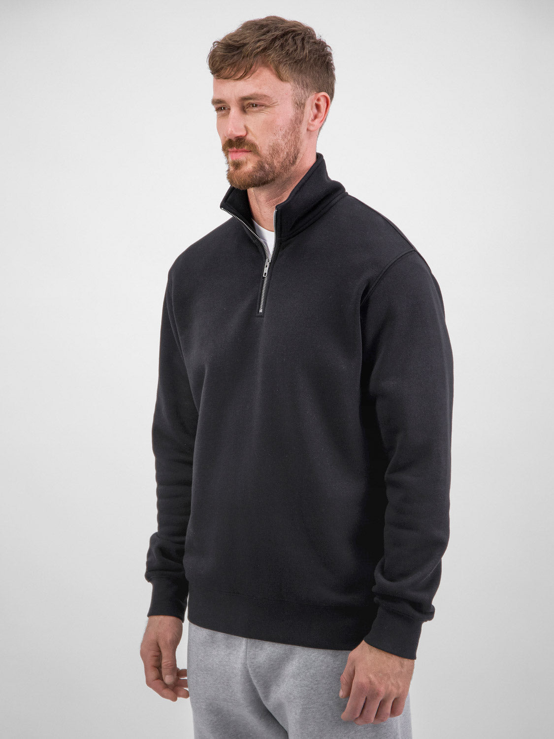 A man wears a black Mens Everyday 1/4 Zip fleece sweatshirt with grey sweatpants.