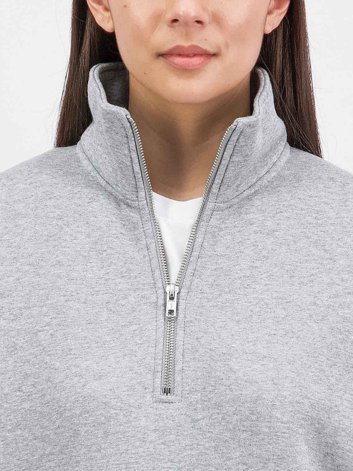 Close-up of a woman wearing a grey marle quarter-zip sweatshirt with a silver metal zipper.