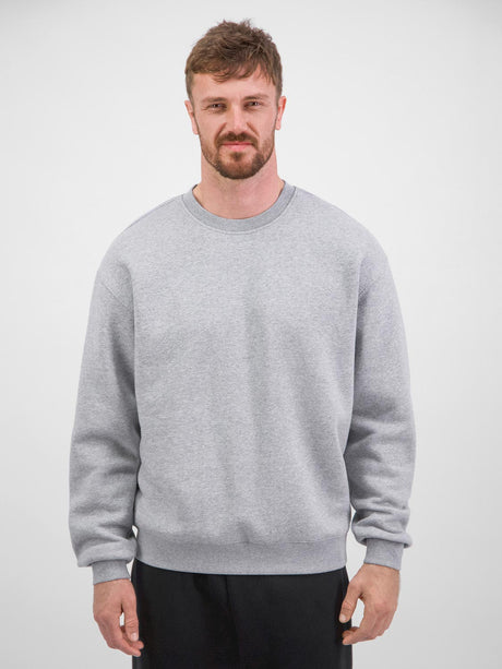 A man wearing a light grey, relaxed-fit crew neck sweatshirt with ribbed cuffs and hem.