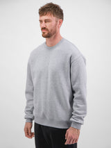 A man wearing a light grey, relaxed-fit crewneck sweatshirt with ribbed cuffs and hem.