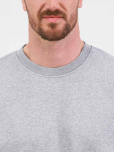 Close-up of a man wearing a grey crew neck sweatshirt with a ribbed collar.