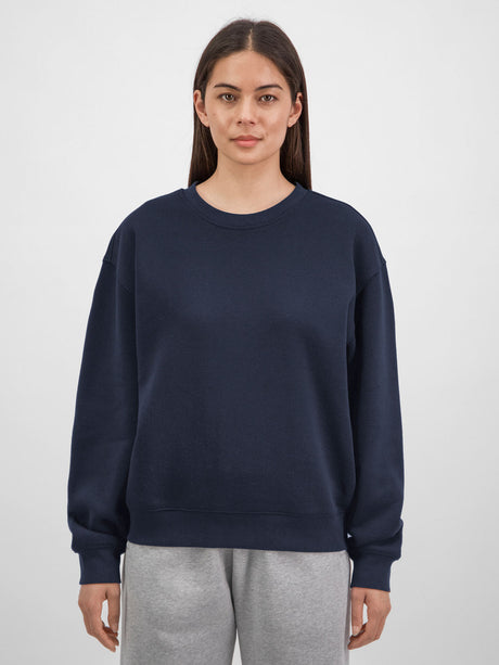 A woman wearing a navy blue crewneck sweatshirt with ribbed cuffs and a relaxed fit.