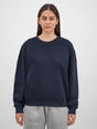 A woman wearing a navy blue crewneck sweatshirt with ribbed cuffs and a relaxed fit.