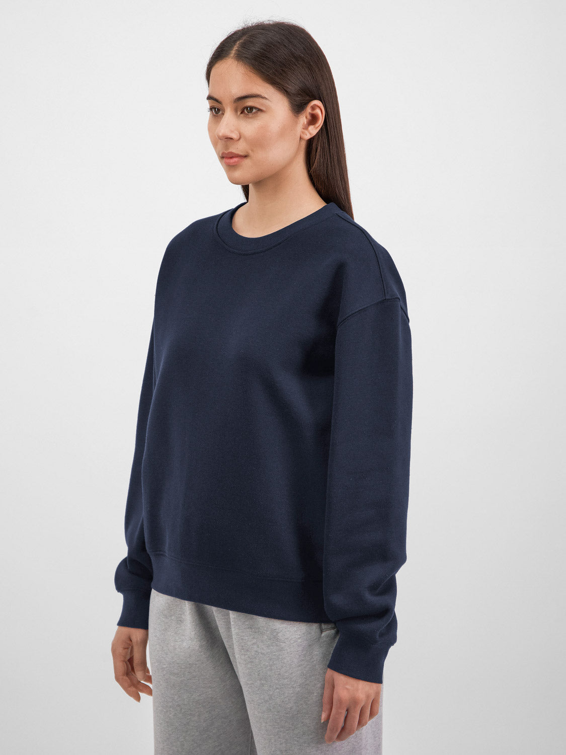 A woman wearing a navy blue crewneck sweatshirt and grey joggers against a white background.