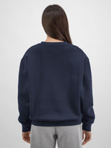 Rear view of a woman wearing a navy blue crewneck sweatshirt with ribbed cuffs and hem.
