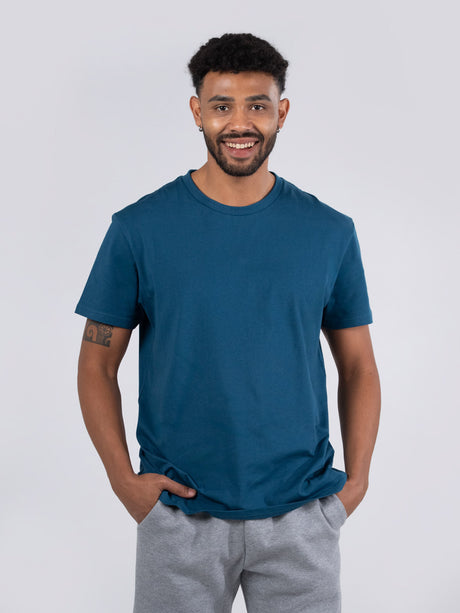 Ramo - A man wearing a teal blue crew neck t-shirt and grey sweatpants against a plain background.