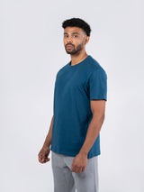 Ramo - A man wearing a teal blue Mens Earth Care T-Shirt and grey sweatpants against a white background.