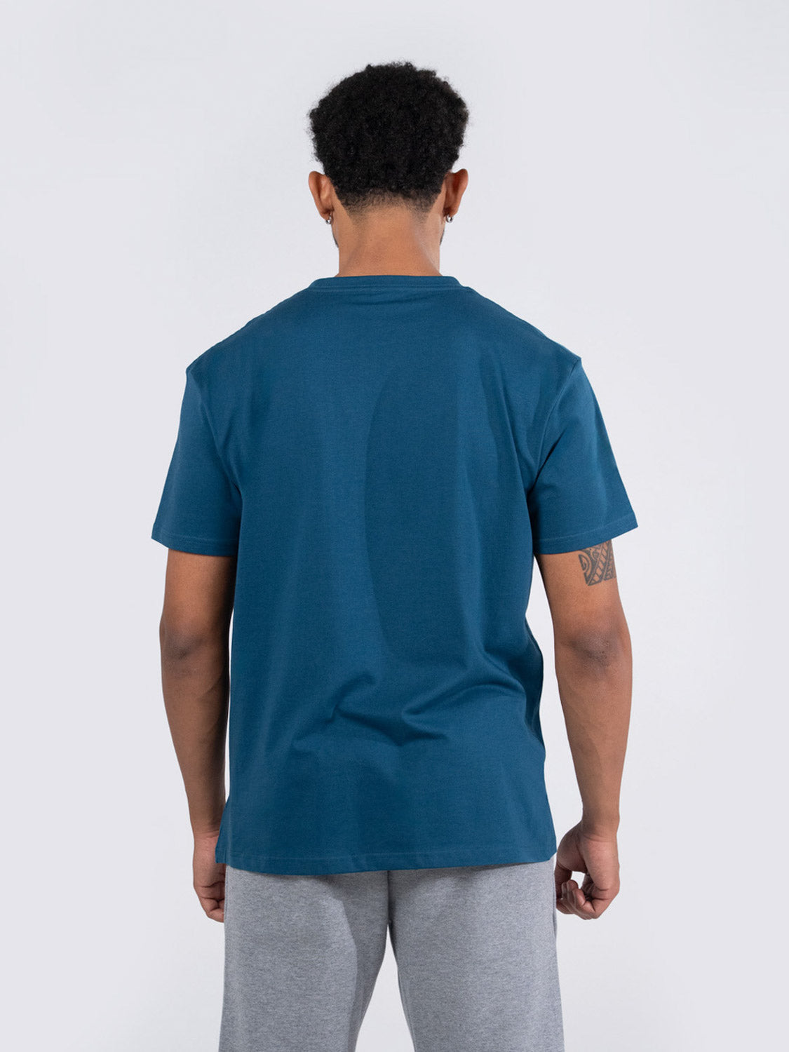 Ramo - Rear view of a man wearing a teal short-sleeve cotton t-shirt and grey shorts.